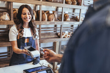 Smiling Bakery Staff Accepts Payment At Counter Using Card Reader In Friendly Shop Scene