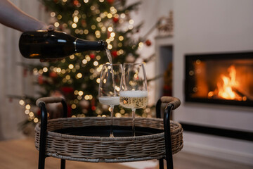 Champagne and glasses on a wicker tray in front of a decorated Christmas tree and fireplace