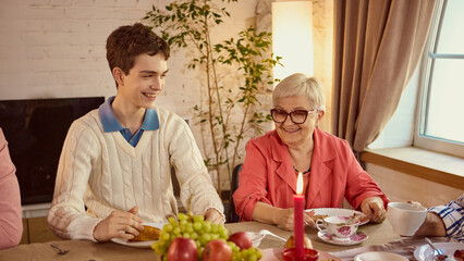 Smiling teenager with grandmother at family dinner table with warm candlelight. Concept of family values, emotional closeness, social campaigns, and generational bond.