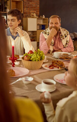 Father in festive sweater smiling during family dinner conversation. Concept of family care, social campaigns, cozy atmosphere, and memory platforms for heritage.