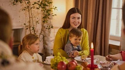Young mother with children smiling warmly at family table. Concept of family happiness, parenting, holiday marketing, cultural values, and platforms of memory and care.