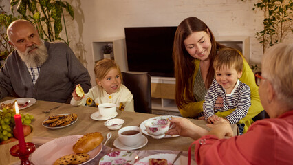 Family generations bonding over cozy dinner with warm smiles. Concept of family care, emotional closeness, cultural holidays, social campaigns, and memory preservation.