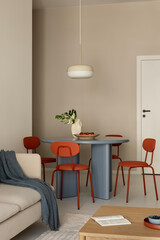Dining area with round blue table, orange chairs and pendant lamp in a modern neutral interior.