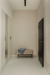 Minimalist hallway with black door, beige walls, upholstered bench and folded blue throw.