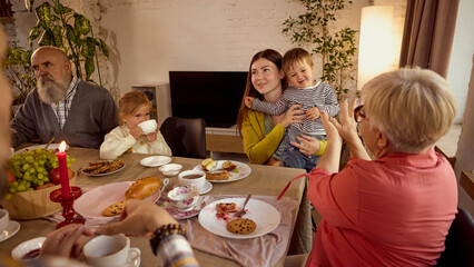Family at festive table with children laughing and sharing food. Concept of warm atmosphere, social campaigns, cultural celebrations, and wellness in everyday joy.