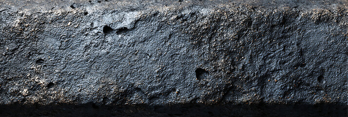 Rough and uneven dark gray stone or concrete texture with visible imperfections and shadows, creating an abstract industrial background.
