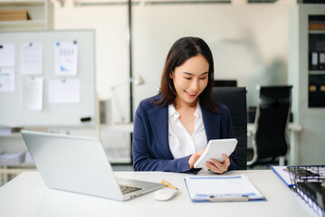 Confident Asian businesswoman using calculator and laptop while smiling in office.