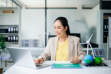 Asian businesswoman in office planning green energy with wind turbine, solar panel, globe. Concept of sustainability, climate change, and reducing CO2 emissions.