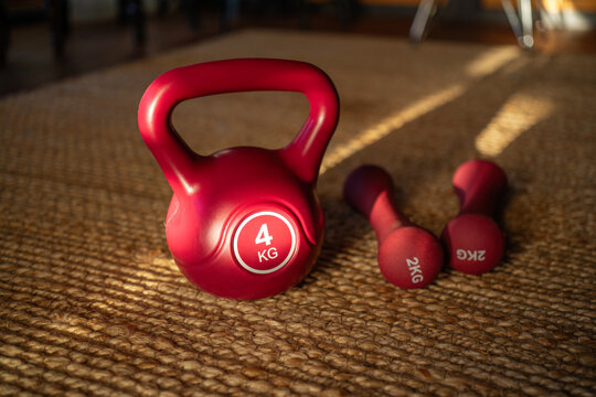 Various weights including a red kettlebell and dumbbells located in a home gym setting during the morning light