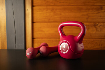 Workout equipment setup with bright red kettlebell and dumbbells on dark surface before evening exercise session