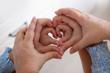 Grandmother, mother and daughter form heart with hands, intergenerational connection female generations, heartwarming image three generations women