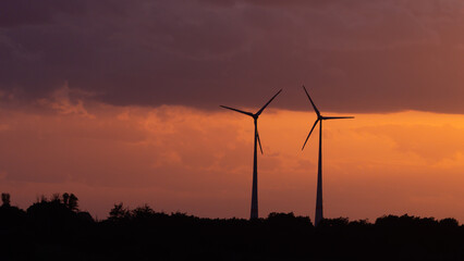 Wind turbines beneath the rain clouds and the striking orange sunset sky