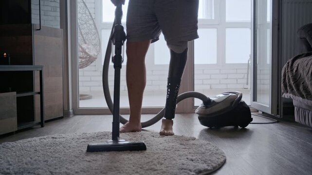 Amputee man with a bionic leg cleaning the floor with a vacuum cleaner during his daily routine