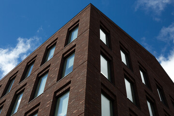 Obraz premium View of modern brick building's corner, showcasing clean geometric facade with horizontal window patterns. The sharp lines and contrast with the sky emphasize the architectural design