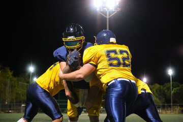 American football players engaging in a tackle during a competitive match under stadium lights at...