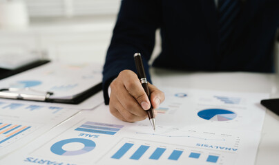 Businessman analyzing financial charts and graphs with a pen while working on reports and calculations at the office.