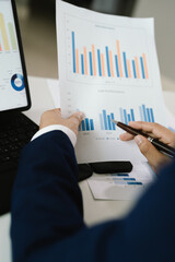 Businessman analyzing financial charts and graphs with a pen while working on reports and calculations at the office.