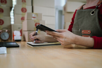 A person using a smartphone and holding a pen while working with packages, symbolizing e-commerce, online business, and order management.