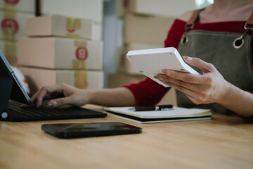 Fototapeta premium A person using a smartphone and holding a pen while working with packages, symbolizing e-commerce, online business, and order management.