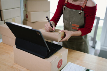A person checking inventory with a tablet and notebook in a warehouse, surrounded by stacked...