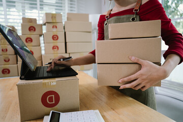 A person checking inventory with a tablet and notebook in a warehouse, surrounded by stacked...