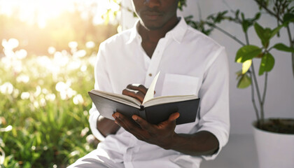 A person in a clean white shirt sits calmly reading a dark-covered book in a sunny garden.