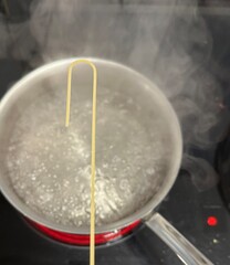 a steel pot of boiling water on the stove with one noodle being interesting