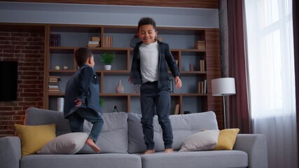 Two little African American kids jumping on couch at living room enjoying relocation moving day in new house funny playful active children sons siblings brothers boys jump on sofa at home playing - Powered by Adobe