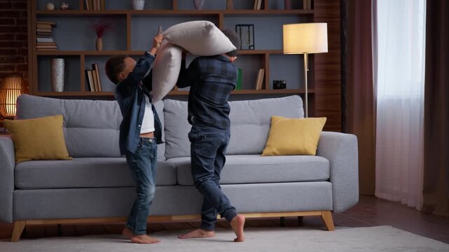 Two playful little African American kids fighting with pillows at home boys siblings brothers sons friends children enjoy fun playing funny fight battle game bit with cushions happiness family play