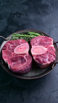 Freshly cut oxtail ready for cooking with herbs on a dark surface