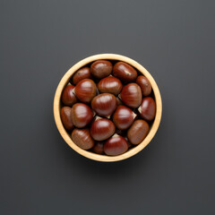 Obraz premium Overhead view of shiny brown chestnuts neatly arranged in a light wooden bowl on a plain grey background, creating a sense of harvest and abundance