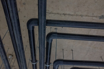 Black industrial pipes with elbow joints fixed to ceiling in modern building, engineering utility system for water, heating, or electricity, technical infrastructure, construction detail, and architec