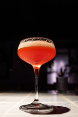 Elegant Red Cocktail in Coupe Glass: Designer's vertical shot of a vibrant, frothy alcoholic beverage on a tile bar counter, perfect for menu design, nightlife, or luxury bar marketing with a dark, mo