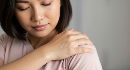 Fototapeta premium Asian woman gently massaging her shoulder with a calm expression 
