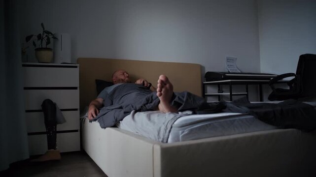Young man with an amputated leg waking up and putting on his artificial limb in his bedroom
