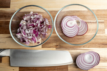 Chopped and sliced red onions on a wooden cutting board with a knife
