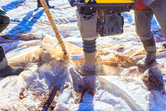 Construction workers use compactor to pack down soil on construction site under works day.