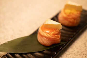 Selective focus of salmon roll with cheese on top on a black plate on stone cutting board in restaurant, Ready to eat or serve