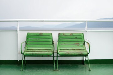 Two weathered green chairs on a ferry deck