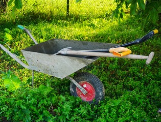 Taczka, łopata i inne narzędzia ogrodowe przygotowane do pracy w ogrodzie na wsi © Adam