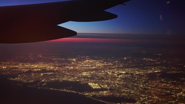 Airplane flying over New York City skyline illuminated at night, with wing view. Jet plane taking off from New York airport at night. Cinematic aerial footage of urban aviation, city lights, USA 