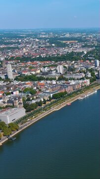 4K vertical drone video glides above Cologne&rsquo;s Rhine waterfront, Koelnmesse halls and city skyline in crisp summer light - premium stock footage for travel, tourism and urban riverfront stories.
