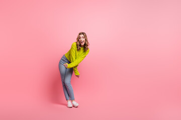Lovely young woman in trendy yellow sweater posing with cheerful energy against a pink backdrop in...