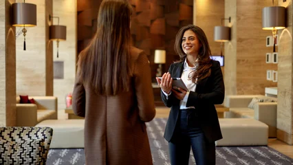 Fotobehang Hotel chique Hotel staff member welcoming guest, offering professional service and hospitality with tablet during check-in  © PeopleVideos