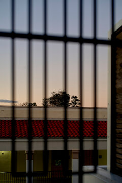 Metal bars frame a view of a building with a red tile roof and trees at sunset. Miami, Florida, USA