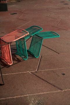 Three colorful wireframe chairs with shadows on a textured stone pavement. Miami, Florida