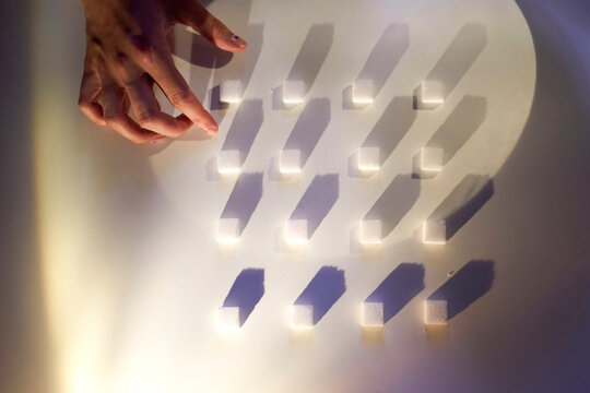 Hand arranging sugar cubes on a white surface with dramatic shadows.