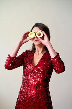Woman in red sequin dress holding avocado halves over her eyes.