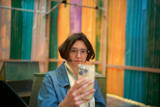 Woman with glasses holding a smartphone in a colorful, vibrant indoor setting. Brussels, Belgium