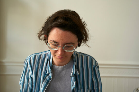 Young woman with glasses and striped shirt looks down against a neutral background. Brussels, Belgium